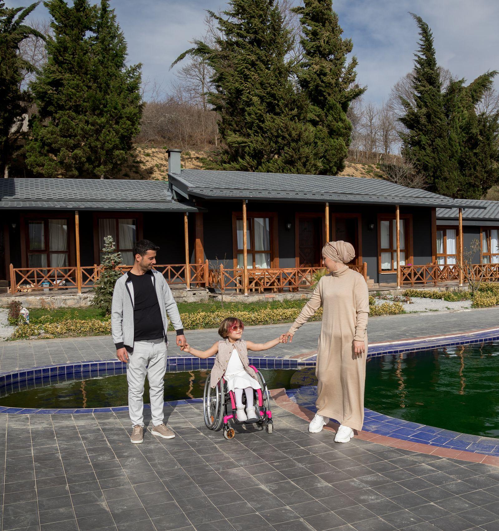 A mother and father at home with their young daughter, who uses a wheelchair